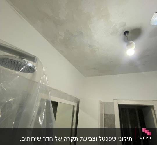 תקרה עם סימני רטיבות ותאורה בחדר אמבטיה